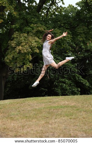 Success and joy for happy slim young woman wearing short dress, jumping into the air outdoors in countryside, enjoying summer sunshine in the forest.