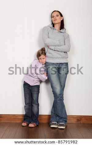 Mother and daughter at home leaning against wall with her shy daughter having a serious family moment. Both wearing denim jeans and hoodie.