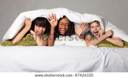 Hilarious fun and scream with laughter at sleepover party for three happy beautiful teenage girl friends, a mixed race african american, oriental Japanese and blonde caucasian school mates.