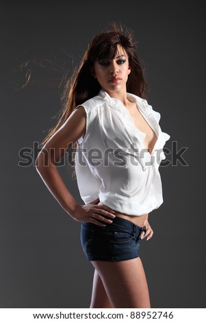 Long hair in wind of beautiful young mixed race fashion model girl wearing denim shorts and white open top, shot against grey background.