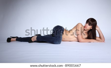 Lying on floor semi nude a sexy young afro caribbean glamour model woman with long brown hair and green eyes, in blue denim jeans showing off long legs wearing black stiletto heels.