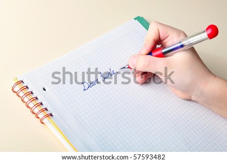 Child\'s hand holding ink pen, while he writes a letter to Santa Claus in checkered workbook asking for Christmas\' gift, \