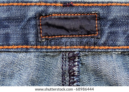 Closeup of blank dark color cotton label inside of blue worn jeans, framed by orange thread, kind of textured background