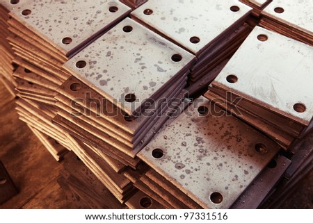 A pile of grungy rusty rectangle metal plates with round holes placed on wooden textured board