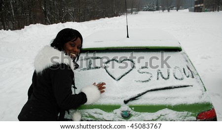 African girl in winter writing on a car window I LOVE SNOW, looking at camera and smiling