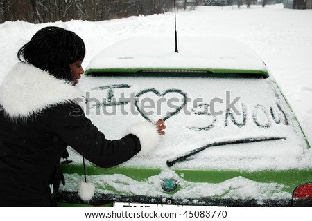 African girl in winter writing on a car window I LOVE SNOW, looking at the car