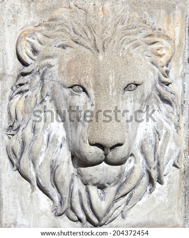 Lion face carved in stone on a wall outside.