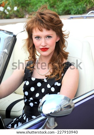 Female beauty fashion model sitting in her classic convertible car.