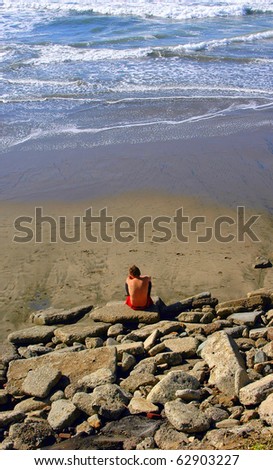 Man sitting on the beach feeling sad and rejected after losing his job.