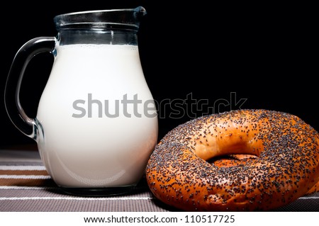 Jug of milk and poppy donuts on dark background