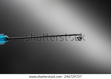Syringe with a droplet coming out of the needle low field of depth studio shot on black background clear liquid medicine or flu vaccination shot drop isolated on black.