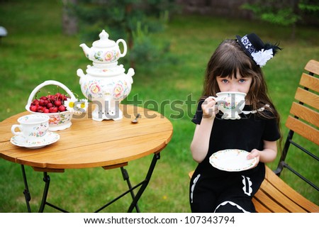 Portrait of elegant child girl in a black dress having a tea party outdoors