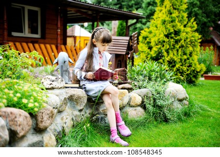 Little girl with pink backpack reading a book outdoors