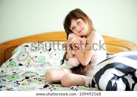 Portrait of little girl sitting in bed with a toy in early morning