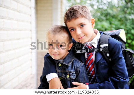 Outdoor portrait of first-grader boy hugging his younger brother