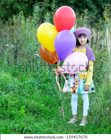 Outdoor portrait of little blue-eyed girl in violet hat holding bunch of balloons