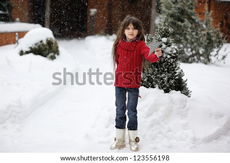 Adorable brunette kid girl with long hair in red sweater plays outdoor in snowfall
