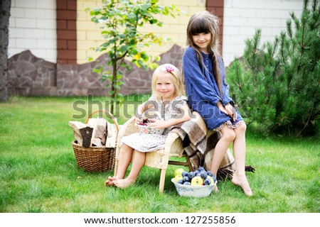 Two happy smiling girls having picnic on a green lawn in front of country house
