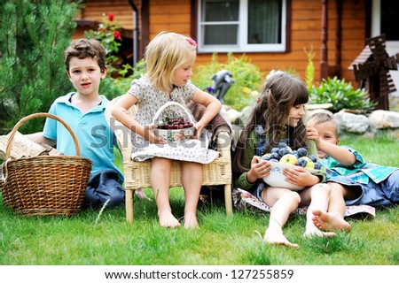 Group of happy children having picnic on a green lawn in front of country house