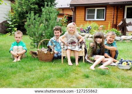 Group of happy children having picnic on a green lawn in front of country house
