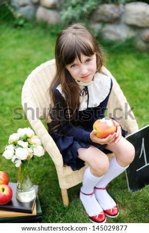 Adorable school girl in navy school uniform with books, chalkboard and apples