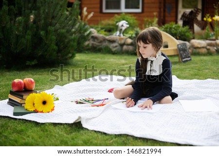 Nice young girl in navy school uniform on white blanket with books and flowers  drawing red apple