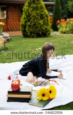 Nice young girl in navy school uniform on white blanket with books and flowers  drawing red apple