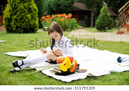 Cute schoolgirl in black and white uniform reading a book in the garden