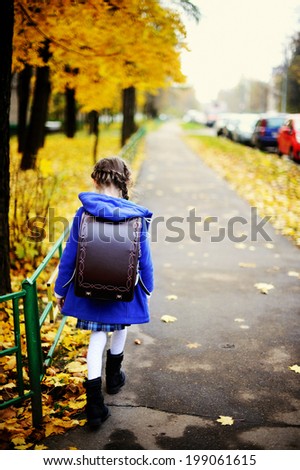 Back to school - adorable brunette girl in blue coat and brown stylish school bag on her way to the school by the autumn city street with yellow trees