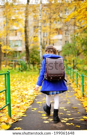 Back to school - adorable brunette girl in blue coat and blue-white school uniform having fun with yellow maple  leaves in the autumn park