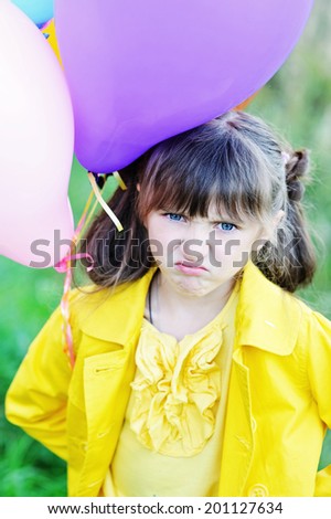 Adorable beauty little girl with funny angry face with bunch of colorful balloons
