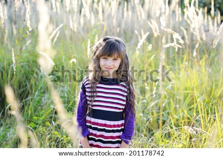 Beauty kid girl in purple knit dress having fun outdoors on warm fall day. Indian summer