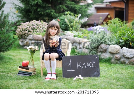 Adorable school girl in navy school uniform with books, chalkboard and apples: on chalkboard sign in russian first grade