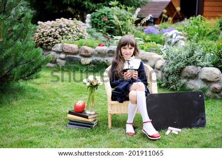 Adorable school girl in navy school uniform with books, chalkboard and apples