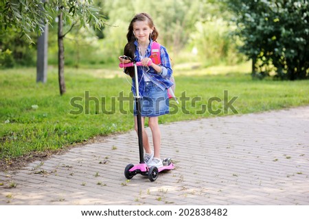 Beauty  fashion brunette school age kid girl in the blue plaid shirt, jeans skirt and yellow scarf writing in her notepad outdoor on the playground