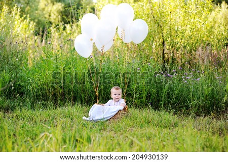 Cute baby boy in the basket with white balloons outdoor in the summer