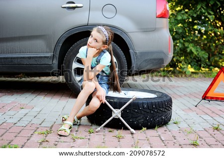 Unhappy kid girl sitting on the wheel and waiting her father to change broken wheel during the family trip