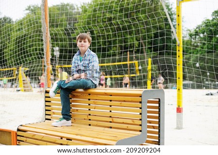 Adorable school age boy watching sport game at the school stadium