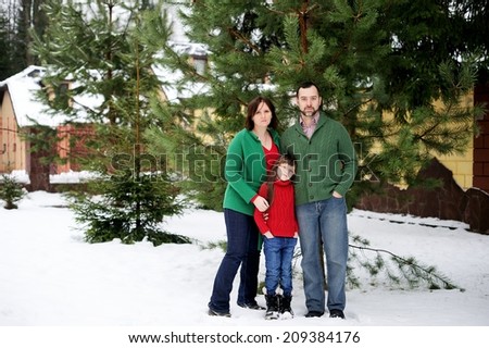 Happy family of three in the red green sweaters outdoor near the house  at the snow winter day