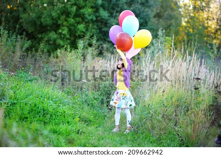 Adorable kid girl in colorful fashion outfit  with bunch of colorful balloons outside at the warm autumn day