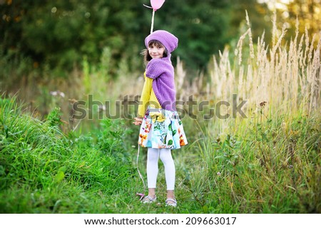 Adorable kid girl in colorful fashion outfit  with bunch of colorful balloons outside at the warm autumn day