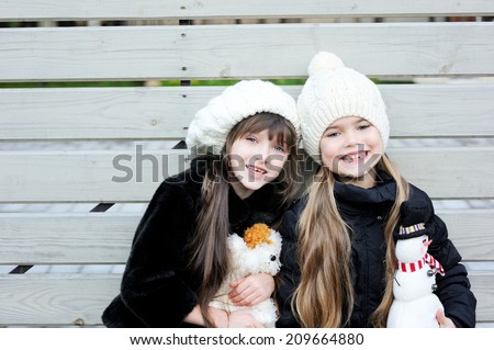 Two adorable kid girl friends in white hats and pattern black jackets has fun outdoor with Christmas lantern at the winter day
