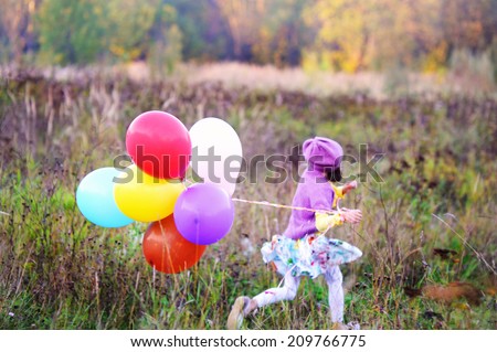 Adorable kid girl in colorful fashion outfit run  with bunch of colorful balloons in the field at the warm autumn day: focus on balloons