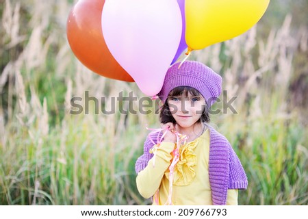 Adorable kid girl in colorful fashion outfit run  with bunch of colorful balloons in the field at the warm autumn day