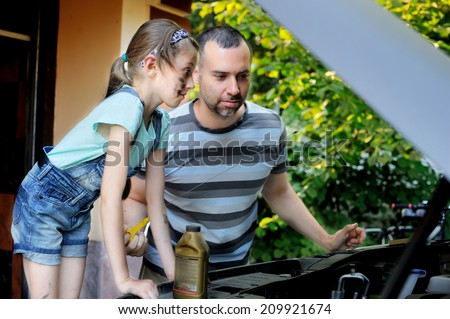 Handsome father teaching his school age daughter to change motor oil in there family car.