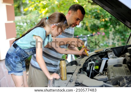 Handsome father teaching his  school age daughter to change motor oil in there family car.