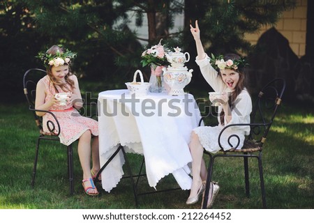 Two adorable kid girls with flower wrearth having tea in the garden. Retro style