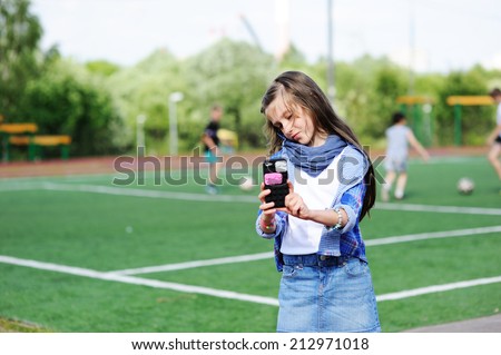 Adorable preteen kid girl making self portrait with funny duck face on her cell phone on the school soccer field