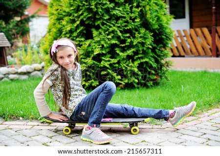 Portrait of a happy fashion kid girl with skateboard in the park