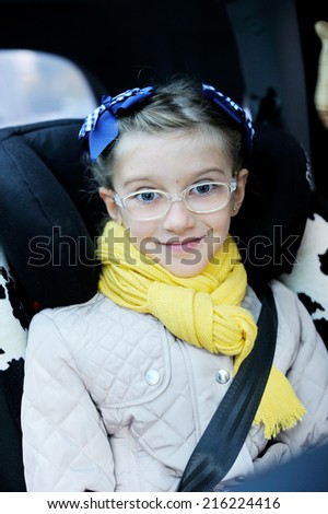 Beauty school aged kid girl in glasses and yellow scarf in the car seat with belt